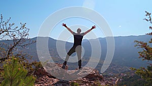Young inspired man raises his hands up standing on the top of a mountain
