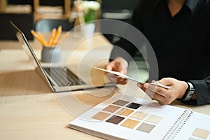 Young interior designer man holding color swatches and using laptop, working for new project at creative office