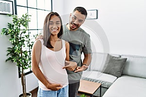 Young interracial couple expecting a baby, touching pregnant belly cheerful with a smile on face pointing with hand and finger up