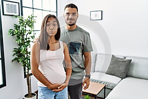 Young interracial couple expecting a baby, touching pregnant belly puffing cheeks with funny face
