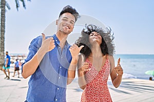 Young interracial couple outdoors on a sunny day success sign doing positive gesture with hand, thumbs up smiling and happy