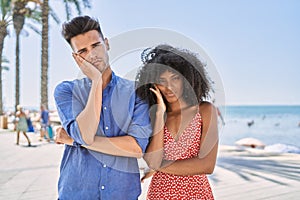 Young interracial couple outdoors on a sunny day thinking looking tired and bored with depression problems with crossed arms