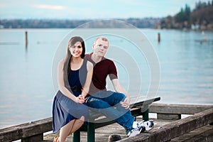 Young interracial couple sitting together on dock over lake