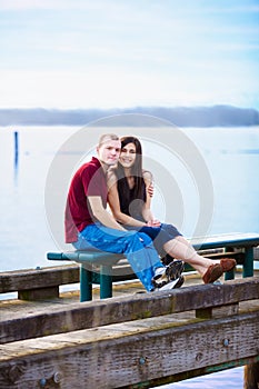 Young interracial couple sitting together on dock over lake