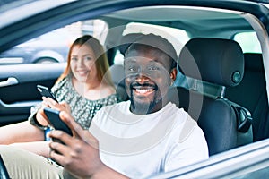 Young interracial couple smiling happy using smartphone at the car