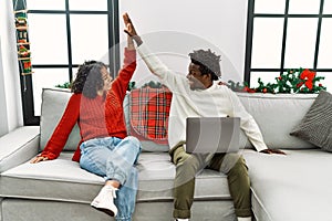 Young interracial couple using laptop and high five sitting on the sofa by at home
