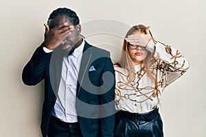 Young interracial couple wearing business and elegant clothes covering eyes with hand, looking serious and sad