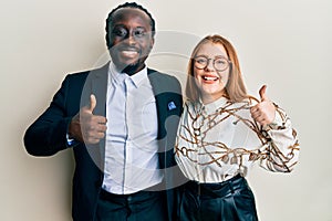 Young interracial couple wearing business and elegant clothes doing happy thumbs up gesture with hand
