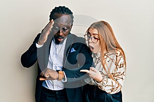 Young interracial couple wearing business and elegant clothes looking at the watch time worried, afraid of getting late