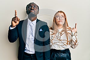 Young interracial couple wearing business and elegant clothes pointing up looking sad and upset, indicating direction with
