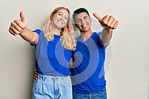 Young interracial couple wearing casual clothes approving doing positive gesture with hand, thumbs up smiling and happy for