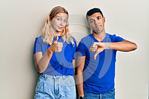 Young interracial couple wearing casual clothes doing thumbs up and down, disagreement and agreement expression