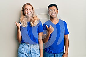 Young interracial couple wearing casual clothes pointing to the back behind with hand and thumbs up, smiling confident