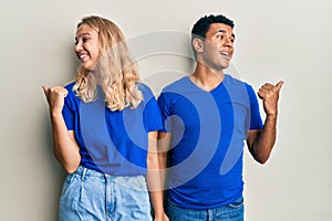 Young interracial couple wearing casual clothes smiling with happy face looking and pointing to the side with thumb up