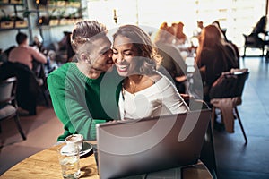 Young interracial lovers spending time in cafe watching media on laptop