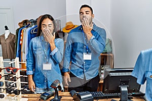 Young interracial people working at retail boutique bored yawning tired covering mouth with hand