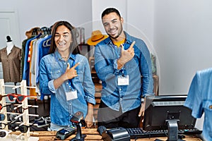 Young interracial people working at retail boutique cheerful with a smile of face pointing with hand and finger up to the side