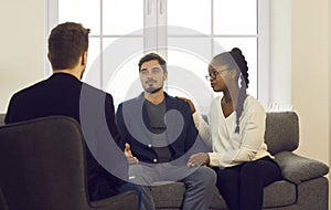 Young interracial spouses talking to man specialist at family consultation