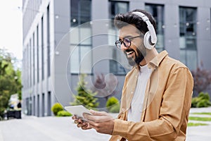 A young Inus man walks around the city in headphones, a businessman in a shirt watches an online video stream using a