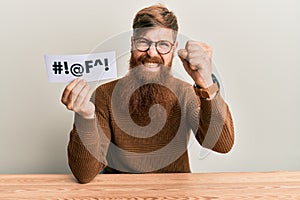 Young irish redhead man holding paper with insult message sititng on the table annoyed and frustrated shouting with anger, yelling