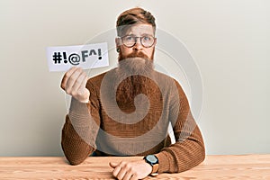 Young irish redhead man holding paper with insult message sititng on the table thinking attitude and sober expression looking self