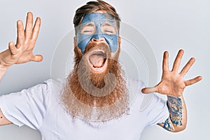 Young irish redhead man wearing facial mask crazy and mad shouting and yelling with aggressive expression and arms raised