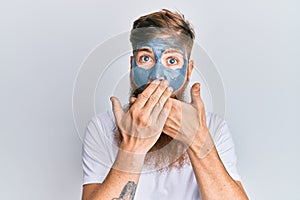 Young irish redhead man wearing facial mask shocked covering mouth with hands for mistake