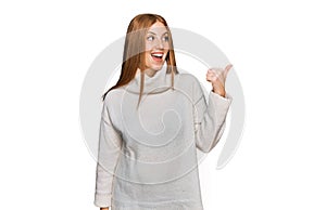 Young irish woman wearing casual winter sweater smiling with happy face looking and pointing to the side with thumb up