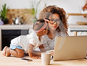 Young irritated african-american mother freelancer trying to work while working remotely with little kid