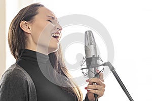 Young Japanese or European woman singing song to microphone in daylight