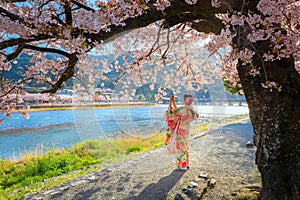 Young Japanese woman in traditional Kimono dress with a full bloom cherry blossom tree and Togetsukyo bridge in Kyoto, Japan