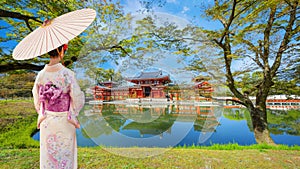 Young Japanese woman in a traditional Kimono dress with the Phoenix Hall of Byodo-in Temple in Kyoto