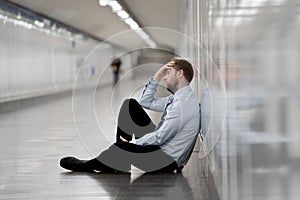 Young jobless business man suffering depression sitting on ground street underground leaning on wall alone looking desperate in