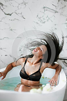 Young jocund girl taking bath and wearing black swimsuit.