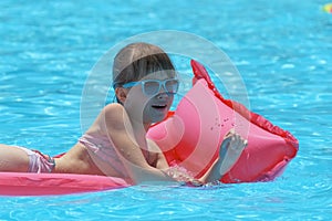 Young joyful child girl having fun swimming on inflatable air mattress in swimming pool with blue water on warm summer