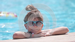Young joyful child girl resting on swimming pool side with clear blue water on sunny summer day. Tropical vacations
