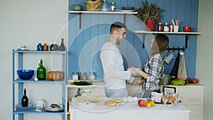 Young joyful couple have fun dancing and singing while set the table for breakfast in the kitchen at home