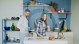 Young joyful couple have fun dancing and singing while set the table for breakfast in the kitchen at home