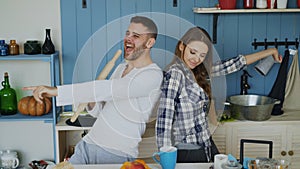 Young joyful couple have fun dancing and singing while set the table for breakfast in the kitchen at home