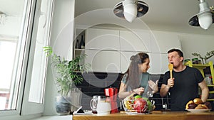 Young joyful couple have fun dancing and singing while set the table for breakfast in the kitchen at home