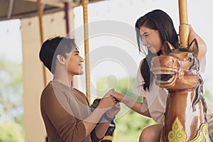 Young joyful couple man and woman riding on horse at Carousel amusement park. Concept happy and lovely life of teenager