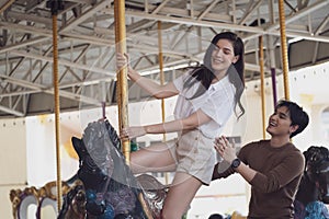 Young joyful couple man and woman riding on horse at Carousel amusement park. Concept happy and lovely life of teenager