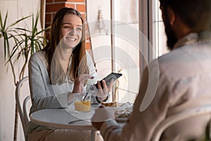 young joyful couple using cellphones and laughing while having breakfast in kitchen at home, bearded man and woman eat