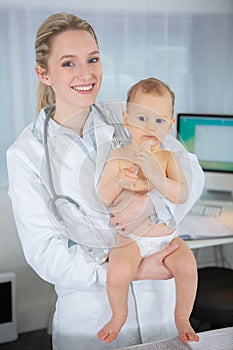 young joyful doctor holding baby and smiling in hospital