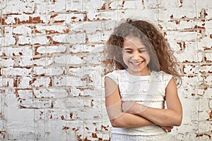 Young joyful girl smiling shyly over a brick wall crossed her arms relaxed