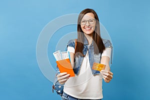 Young joyful happy woman student in glasses with backpack hold passport boarding pass ticket credit card isolated on