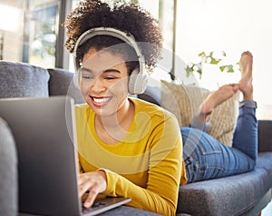Young joyful mixed race woman wearing headphones and listening to music while using a laptop at home. One happy hispanic
