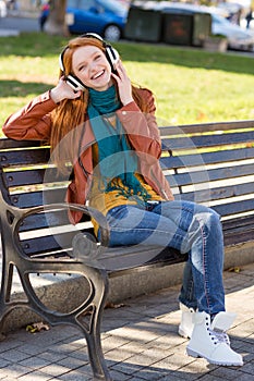 Young joyful pleased female listening to music in the park