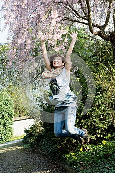Young joyful woman jumps under flowering tree