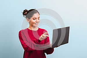 Young joyful woman student with beautiful smile holding an opened laptop and about to press a key on keyboard. investing in